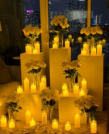 Elegant arrangement of white roses and glowing candles against a city night backdrop.