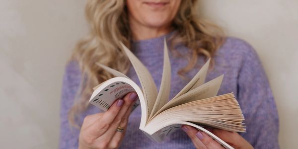 Woman flipping through a book with a smile, wearing a purple sweater.