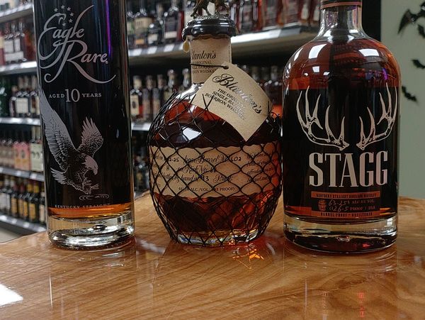 Three bottles of premium bourbon whiskey on a wooden counter in a liquor store.
