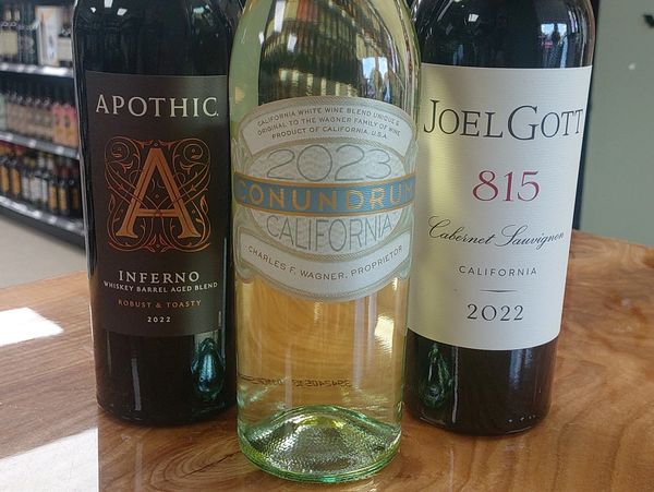 Three bottles of California wine displayed on a wooden surface in a liquor store.