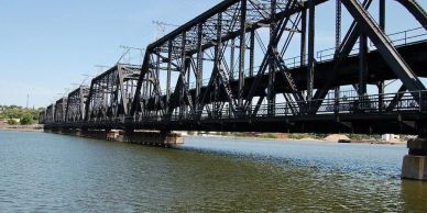 Steel truss bridge over calm water under clear sky.