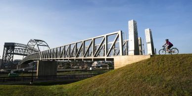 A person biking near a large steel bridge on a sunny day.