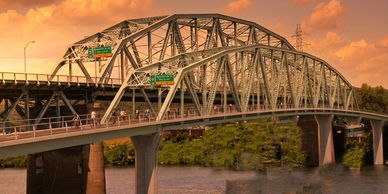 A metal bridge at sunset with traffic and pedestrians.