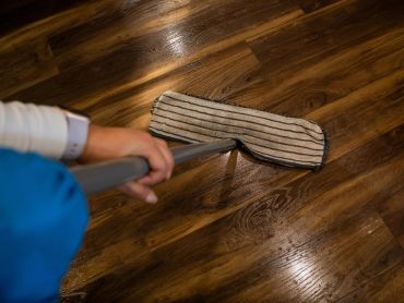 Persona limpiando un piso de madera con trapeador.