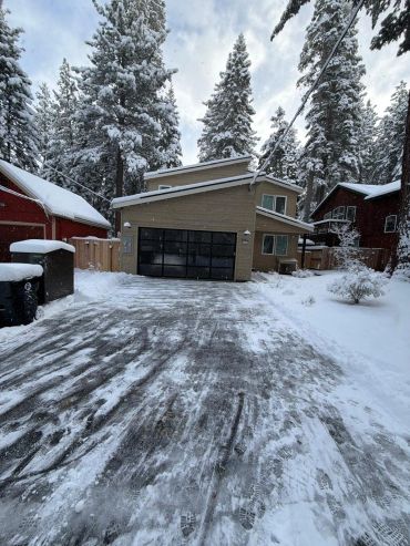 Casa moderna con nieve y pinos altos alrededor.