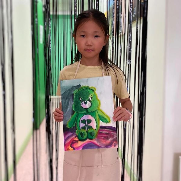 Young girl holding a drawing of a green bear.