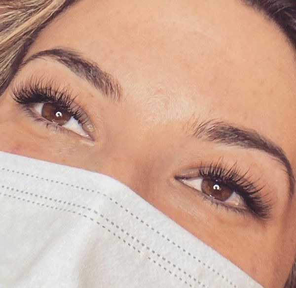 Close-up of brown eyes with long lashes above a white face mask.