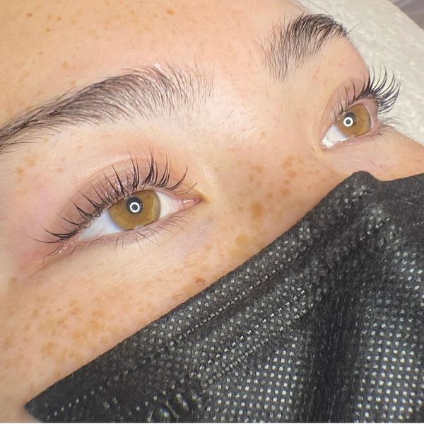 Close-up of eyes with long lashes and freckles, wearing a black mask.
