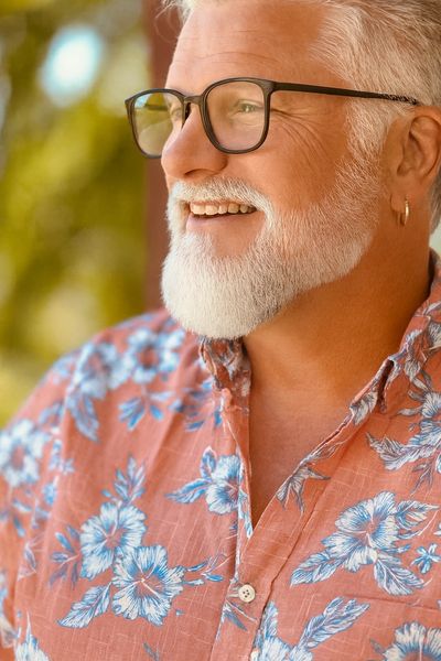 Smiling elderly man with white beard and glasses in a floral shirt.