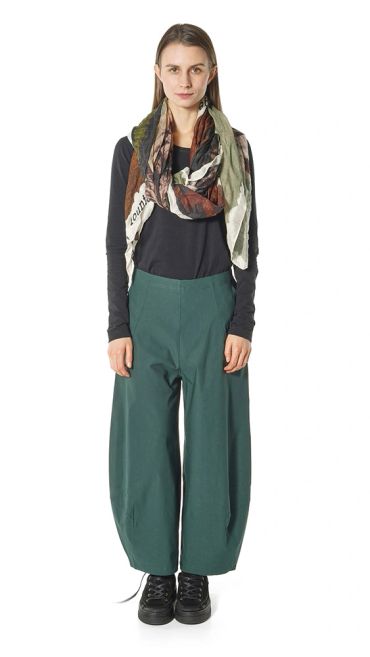 Woman wearing a green scarf, black top, and green wide-legged pants.