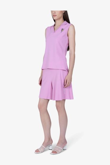 Woman wearing a pink sleeveless top and matching shorts with white heels.