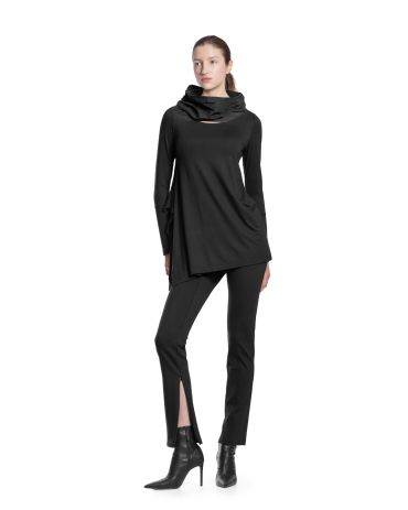 Femme posant en tenue noire élégante avec pantalon fendu et bottines à talons.