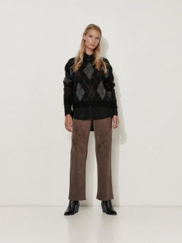 Femme portant un pull noir à motif losange et un pantalon marron.