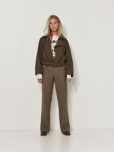 Femme debout en pantalon marron et veste kaki.