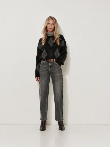 Femme portant un pull à losanges et un jean gris.