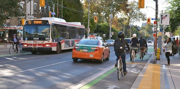 Urban street with cyclists, a bus, and a taxi navigating traffic.