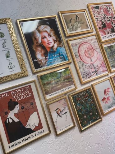 A wall decorated with various framed art and vintage posters in gold frames.
