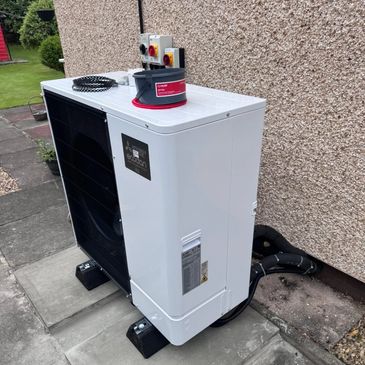 A white outdoor heat pump unit installed next to a house wall.