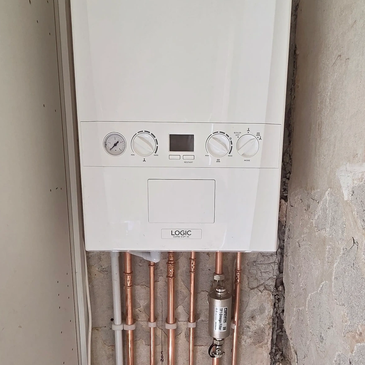 Wall-mounted boiler with copper pipes and control dials.