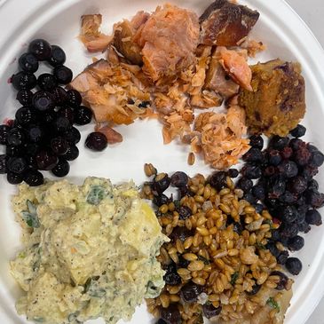 A plate with scrambled eggs, cooked salmon, berries, and a grain salad.