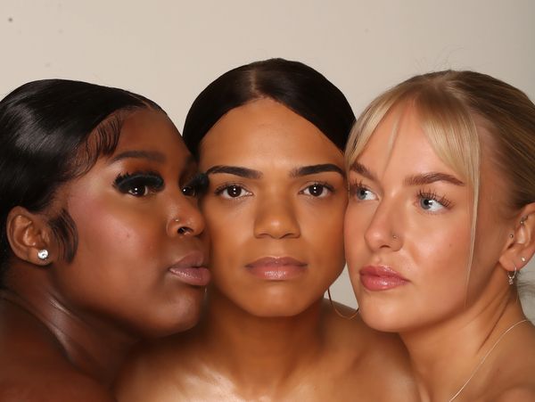 Three diverse women pose closely together against a neutral background exposing the benefits of botanical skincare products. 