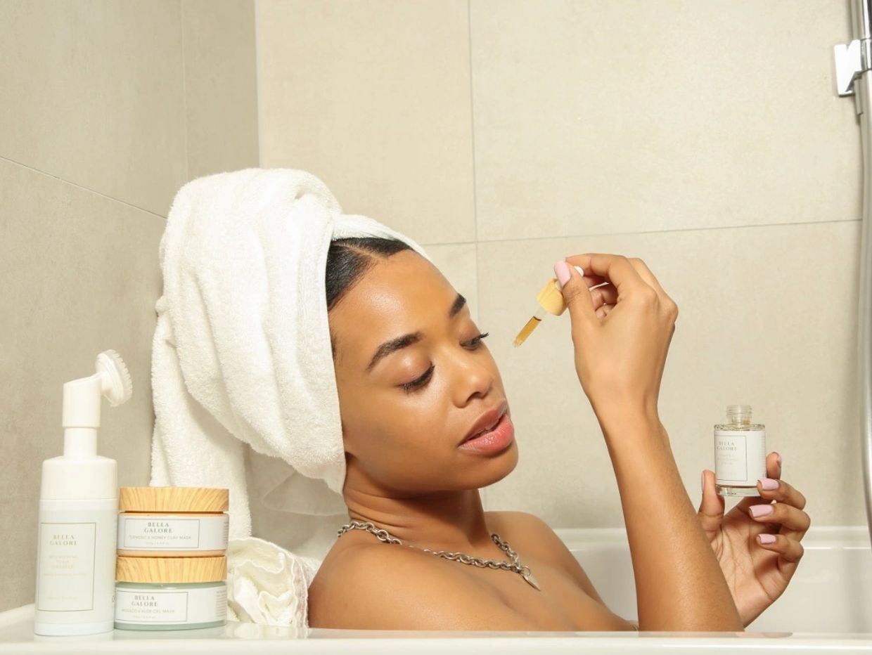 Woman in bathtub using facial serum with towel on her head.