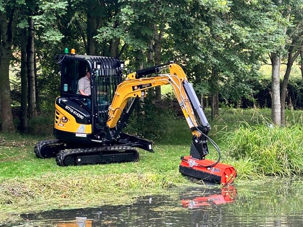 Digger with attachment trimming plants around pond area
