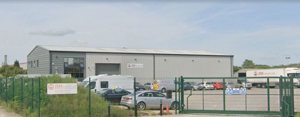 Industrial warehouse with parked vehicles and gated entrance.