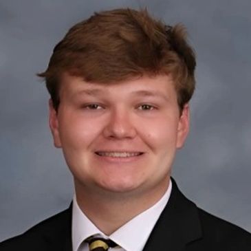 Young man in formal attire smiling against a gray backdrop.