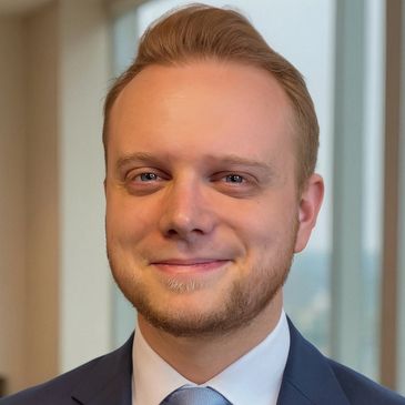 Professional young man in a suit smiling warmly indoors.