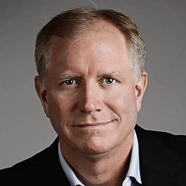 Portrait of a middle-aged man in formal attire against a gray background.