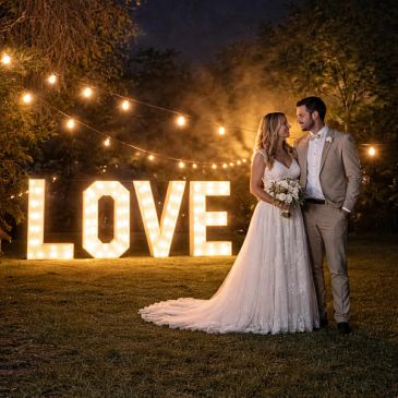 Bride and groom standing by illuminated LOVE sign at night.