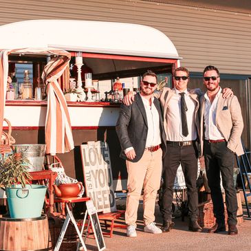 Three men posing happily in front of a decorated Hello Mr Jenkins vintage van.