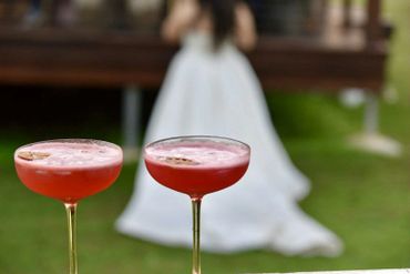 Two red cocktails with a blurred bride in the background outdoors.