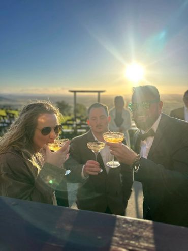 Three people enjoying drinks outdoors at sunset, dressed formally.