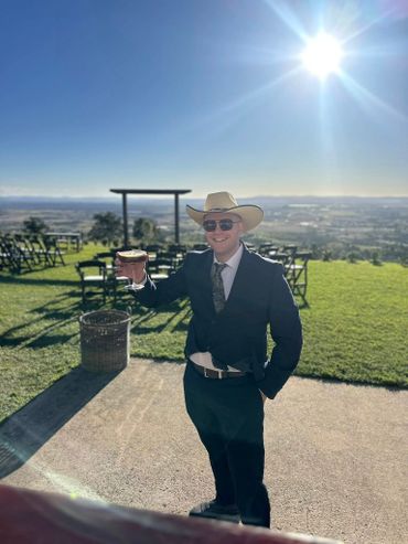 Man in suit and cowboy hat holding a drink outdoors on a sunny day.