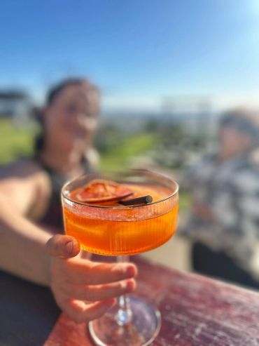 Person holding a vibrant orange cocktail outdoors with blurred background.