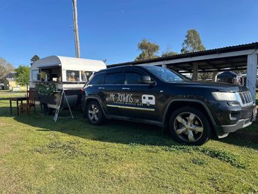 Black SUV parked beside a vintage mobile bar trailer on a sunny day.