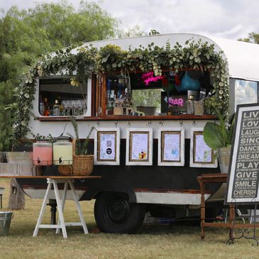 Vintage caravan bar decorated with greenery and inspirational sign outdoors.