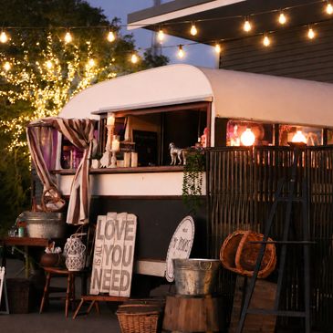 Cozy outdoor food truck decorated with string lights and rustic signs at dusk.