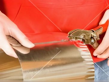 Hands using metal shears to precisely cut a piece of sheet metal.