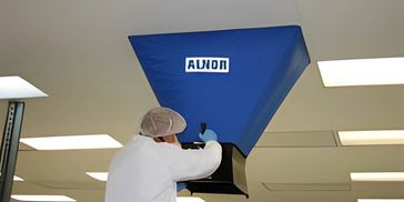 A technician using a blue capture hood to measure airflow from a ceiling vent.