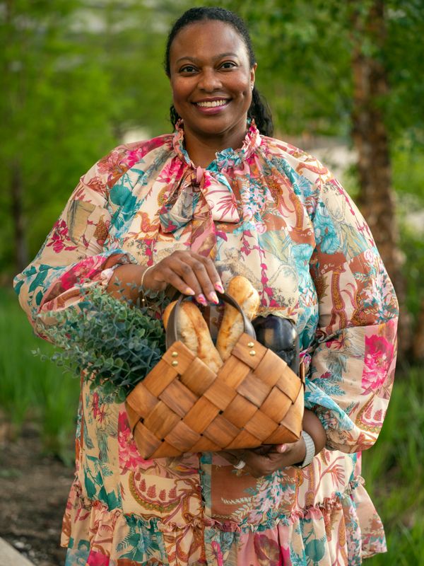 Smiling woman outdoors holding a basket with bread and greenery.