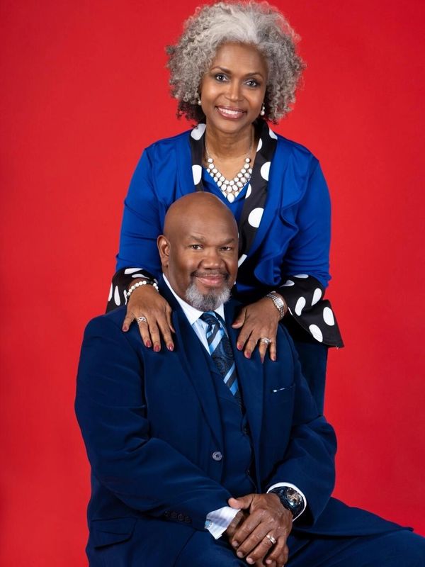 A mature couple dressed in blue poses warmly against a red background.