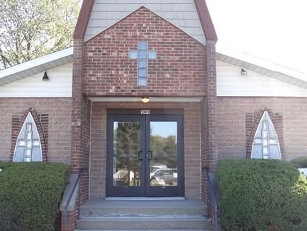 Entrance of a small brick church with a cross above the door.
