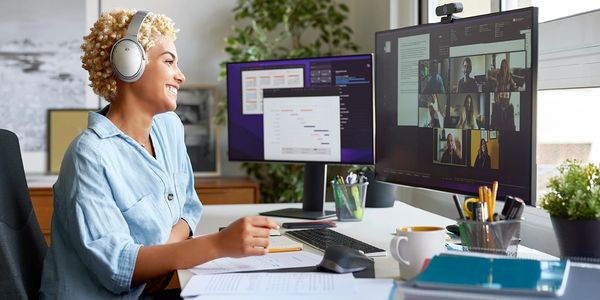 Woman with headphones engaged in a virtual meeting at her desk with dual monitors.