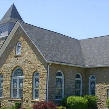 Stone church building with arched windows and a steeple.