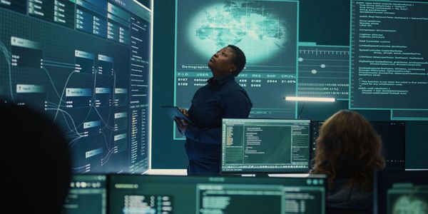 Woman analyzing data on large digital screens in a tech control room.