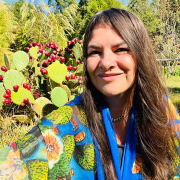 Woman smiling outdoors with cactus plants bearing red fruit in the background.