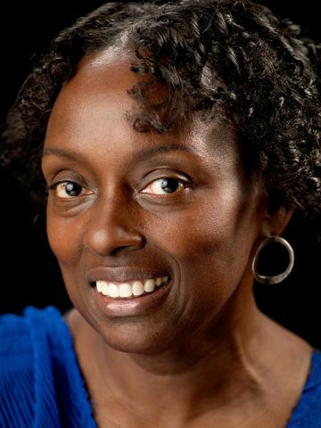 Smiling woman with curly hair wearing a blue top and hoop earrings.